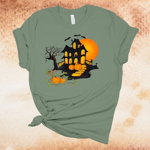 May include: A green t-shirt with a black silhouette of a haunted house with a full moon and pumpkins in front of it.