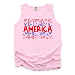 May include: A pink sleeveless tank top with the word "AMERICA" repeated five times in red and blue letters. The letters are stacked on top of each other, with each word slightly offset from the one above it.