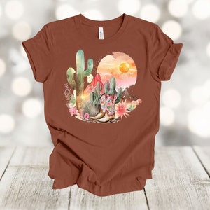 Camiseta gráfica Atardecer en el desierto: Camiseta estilo vaquero con estampado de cactus y botas. Terracotta