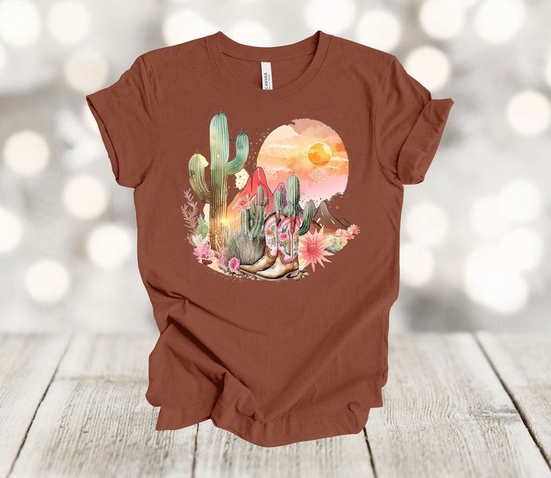 Camiseta gráfica Atardecer en el desierto: Camiseta estilo vaquero con estampado de cactus y botas. Terracotta