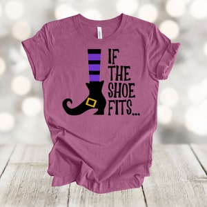 May include: A mauve t-shirt with a black witch's shoe and the text "If the shoe fits..."