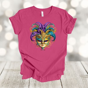 May include: A pink t-shirt with a gold, blue, and purple masquerade mask graphic.