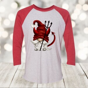 May include: A red and white baseball tee shirt with a cartoon image of a gnome with a red hat and a devil tail and pitchfork.