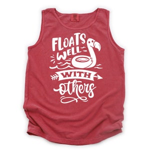 May include: Red sleeveless tank top with white text that reads "Floats Well With Others" and a flamingo with a pool float.