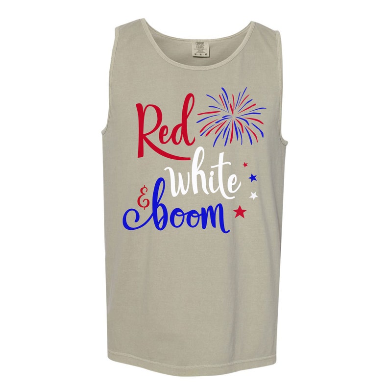 Puede incluir: Una camiseta sin mangas de color gris claro con el texto "Red, White & Boom" en letras rojas, blancas y azules. Un gr&aacute;fico de fuegos artificiales rojo, blanco y azul est&aacute; por encima del texto.