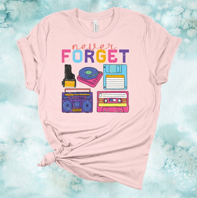 May include: Pink t-shirt with the text "never FORGET" in colourful letters. The shirt features a retro design with images of a cassette tape, a record player, a boombox, and a floppy disk.
