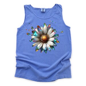 May include: A blue tank top with a colorful, iridescent daisy graphic. The daisy has a white center and petals with a rainbow sheen.