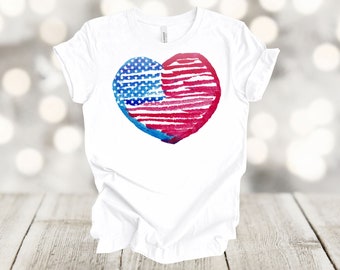 Puede incluir: Camiseta blanca con un diseño de corazón de acuarela rojo, blanco y azul con la bandera estadounidense.