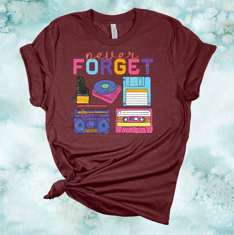 May include: A maroon t-shirt with the text "never FORGET" in rainbow colours. The shirt features a graphic of vintage music technology, including a cassette tape, a boombox, a floppy disk, a record player, and a camera.