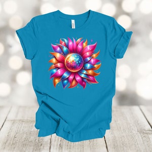 May include: A turquoise blue t-shirt with a colorful flower design. The flower has pink, orange, and blue petals with a silver disco ball in the center.