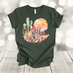 Camiseta gráfica Atardecer en el desierto: Camiseta estilo vaquero con estampado de cactus y botas. Heather Forest