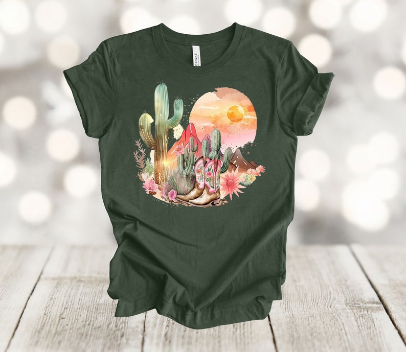 Camiseta gráfica Atardecer en el desierto: Camiseta estilo vaquero con estampado de cactus y botas. Heather Forest