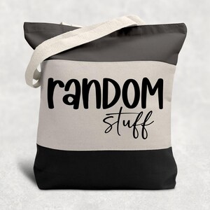 May include: A black, white, and gray tote bag with cream-colored handles. The bag features the words "random stuff" in black script across the front. The bag is divided into three horizontal sections of color.