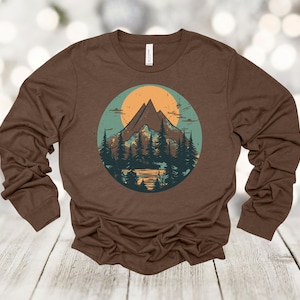May include: A brown long-sleeve shirt with a vintage-style graphic of a mountain range with a sun and trees in a circle.