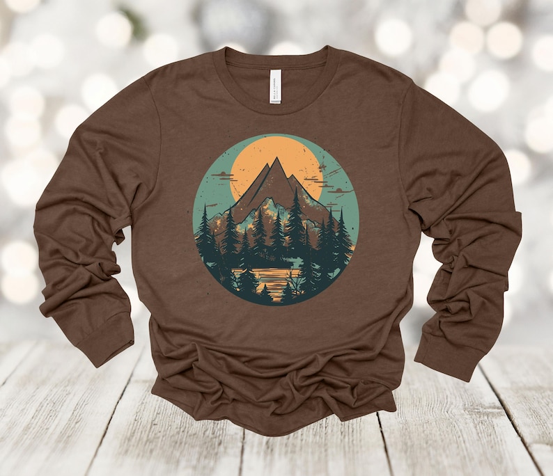 May include: A brown long-sleeve shirt with a vintage-style graphic of a mountain range with a sun and trees in a circle.
