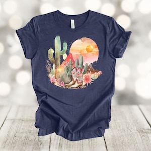Camiseta gráfica Atardecer en el desierto: Camiseta estilo vaquero con estampado de cactus y botas. Heather Navy