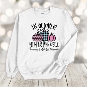 May include: White sweatshirt with the text "In October We Wear Pink & Blue" and a graphic of three pumpkins. The text "Pregnancy & Infant Loss Awareness" is below the pumpkins.