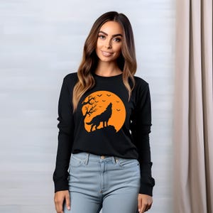 May include: Black long-sleeved shirt with an orange and black wolf howling at the moon graphic. The moon is surrounded by bats.