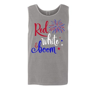 Puede incluir: Una camiseta sin mangas gris con el texto "Red, White & Boom" en letras rojas, blancas y azules. Un gr&aacute;fico de fuegos artificiales rojo, blanco y azul est&aacute; al lado del texto.