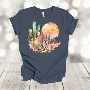 Camiseta gráfica Atardecer en el desierto: Camiseta estilo vaquero con estampado de cactus y botas. Vintage Navy
