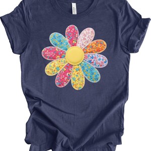 May include: Navy blue t-shirt featuring a large, colorful flower design. The flower has petals in various colors, including pink, yellow, blue, and orange, with a yellow center. The petals have floral patterns. The shirt is made of soft material.
