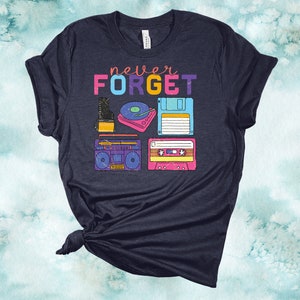 May include: A navy blue t-shirt with the text "never FORGET" in rainbow colours. The shirt features a graphic of vintage technology, including a cassette tape, a floppy disk, a record player, and a boombox.