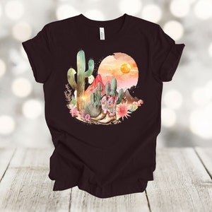 Camiseta gráfica Atardecer en el desierto: Camiseta estilo vaquero con estampado de cactus y botas. Oxblood