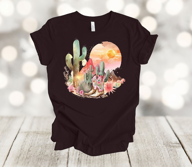 Camiseta gráfica Atardecer en el desierto: Camiseta estilo vaquero con estampado de cactus y botas. Oxblood