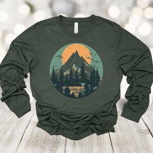May include: A dark green long-sleeved t-shirt with a vintage-style graphic of a mountain range with a sunset behind it. The graphic is in a circle with a light blue background.