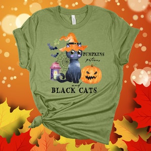 May include: Green t-shirt with a black cat wearing a witch hat, a pumpkin, and a lantern. The text on the shirt reads "Pumpkins potions and BLACK CATS".