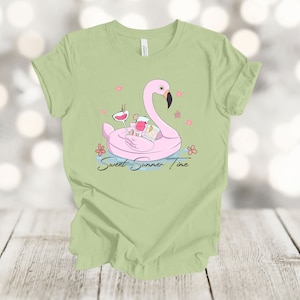 May include: A light green t-shirt with a pink flamingo pool float with two cocktails and the text "Sweet Summer Time" printed on the front.