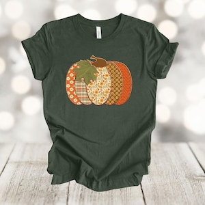 May include: A dark green t-shirt with a patchwork pumpkin design. The pumpkin is made up of different fabrics with floral and plaid patterns in shades of orange, brown, and white.