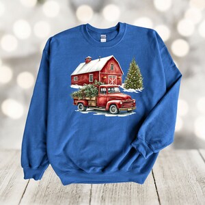 May include: A red pickup truck with a Christmas tree in the back, driving past a red barn with a snowy roof. The truck and barn are in front of a snowy background.