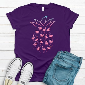 May include: Purple t-shirt with a pink and blue ombre pineapple design featuring pink flamingo silhouettes.