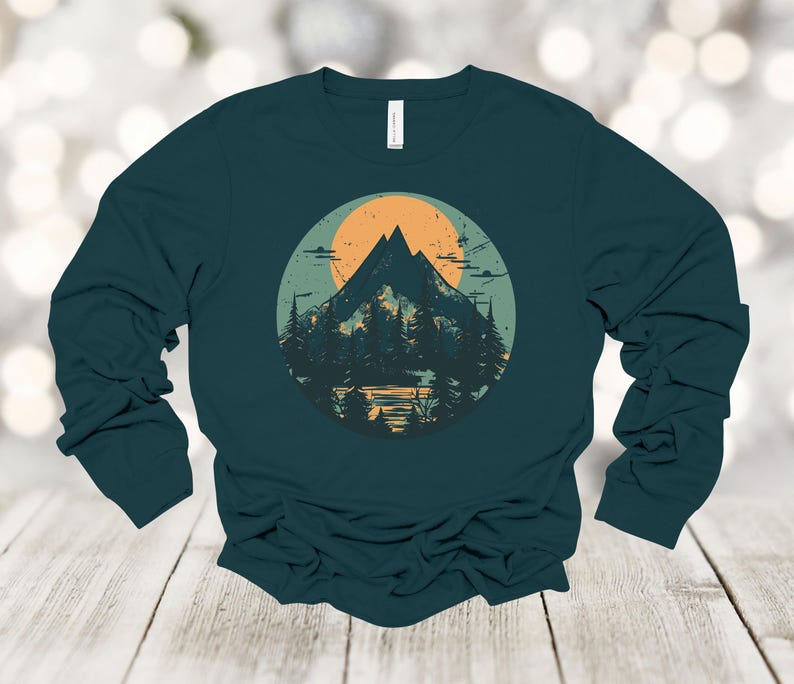 May include: A teal long-sleeve shirt with a graphic of a mountain range and a sun in a circle. The mountains are green and brown, and the sun is orange.