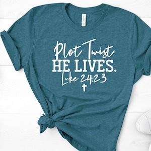 May include: Teal blue t-shirt with white text that reads "Plot Twist He Lives. Luke 24:23" and a white cross.