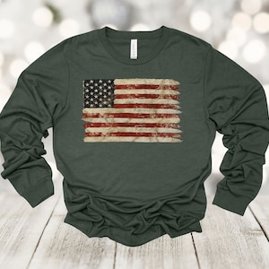 May include: A dark green long-sleeved t-shirt with a distressed American flag design printed on the front.
