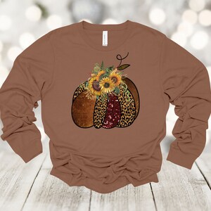 May include: A brown long-sleeved shirt with a graphic of a pumpkin decorated with sunflowers and leopard print.