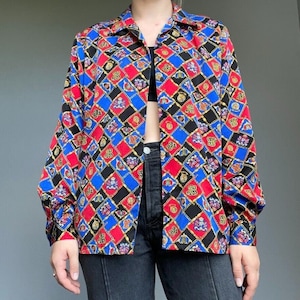May include: A long-sleeved button-up shirt with a colorful geometric pattern. The pattern features red, blue, black, and gold colors and includes a repeating design of chains and crests.