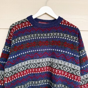 May include: A blue, red, and white patterned sweater with a crew neck.
