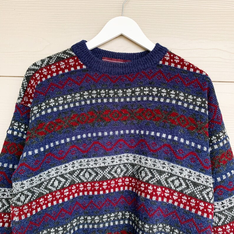 May include: A blue, red, and white patterned sweater with a crew neck.