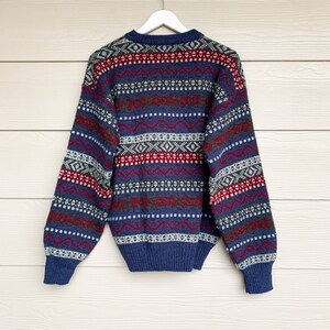 May include: A blue, red, and white patterned sweater with long sleeves. The sweater has a crew neck and is made of a soft, knitted fabric.