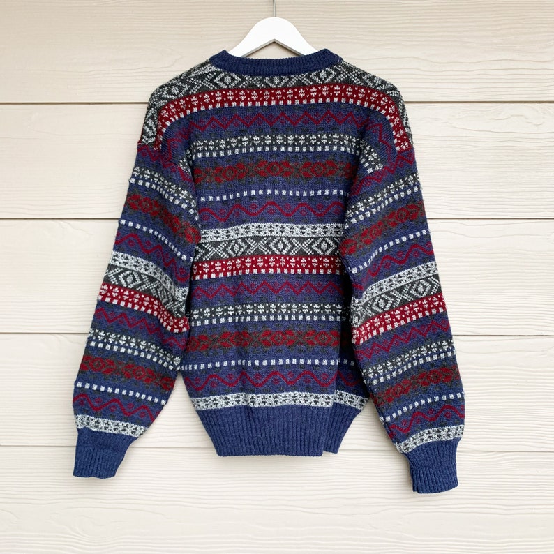 May include: A blue, red, and white patterned sweater with long sleeves. The sweater has a crew neck and is made of a soft, knitted fabric.