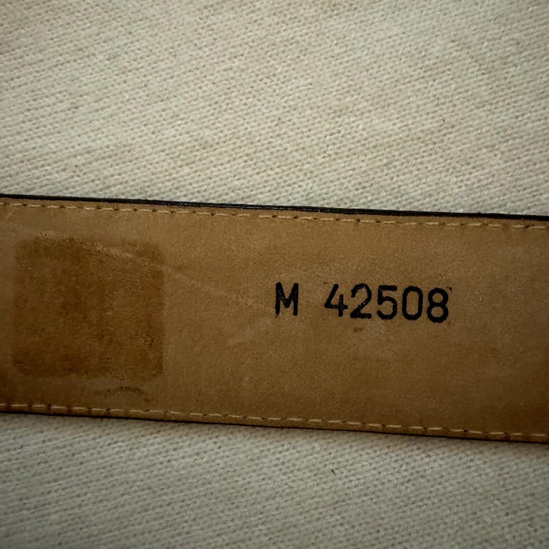 Puede incluir: Primer plano de un cintur&oacute;n de cuero marr&oacute;n con el texto "M 42508" grabado en el interior.