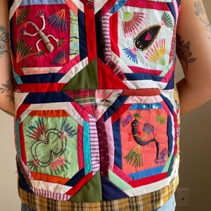 May include: A colorful patchwork vest with embroidered designs of a lizard, a snake, and a flower. The vest is made of different fabrics and colors, including red, blue, green, and white.