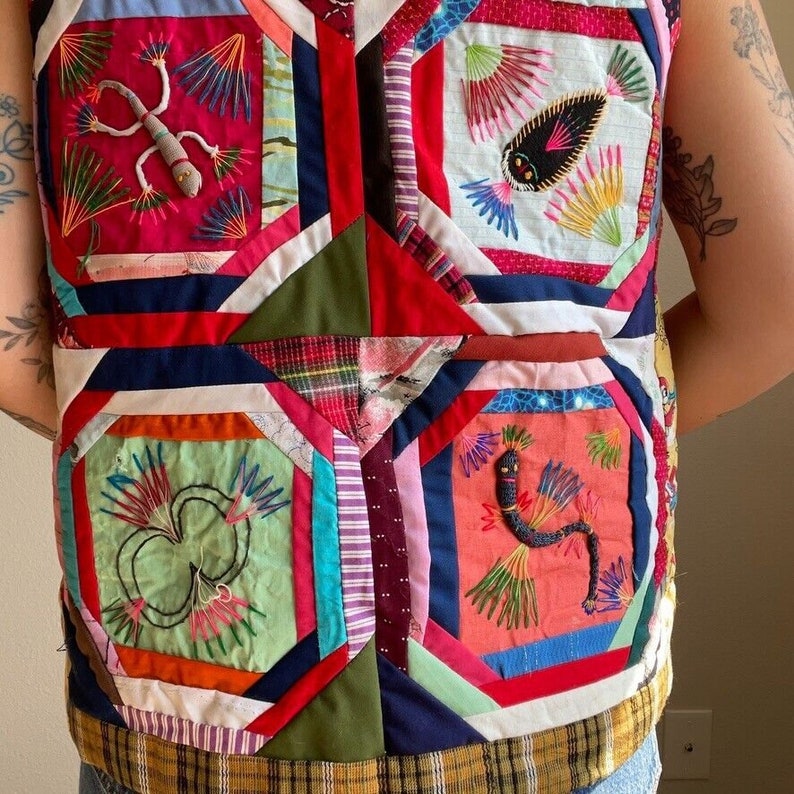 May include: A colorful patchwork vest with embroidered designs of a lizard, a snake, and a flower. The vest is made of different fabrics and colors, including red, blue, green, and white.