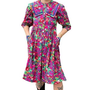 May include: A pink floral dress with a blue and white sailor collar. The dress has a button-up front and pockets on the sides.