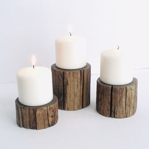 Peut inclure: Trois bougies blanches en forme de pilier sur des bougeoirs en bois rustique. Les bougeoirs sont en bois naturel avec une texture rugueuse.