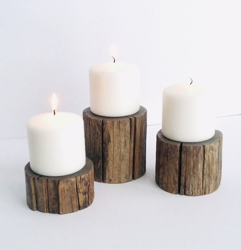 Peut inclure: Trois bougies blanches en forme de pilier sur des bougeoirs en bois rustique. Les bougeoirs sont en bois naturel avec une texture rugueuse.