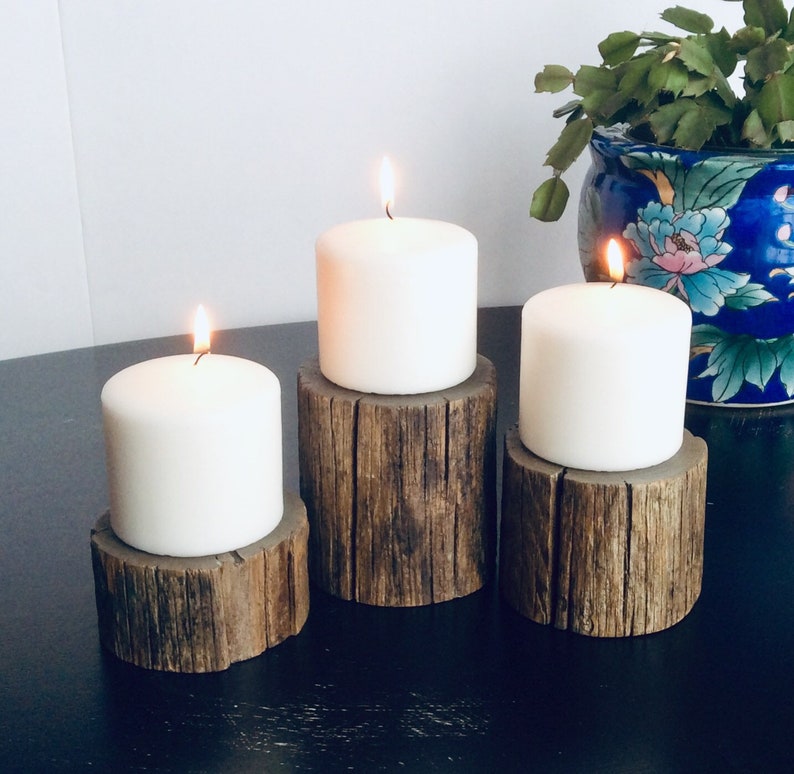 Peut inclure: Trois bougies blanches en forme de pilier sur des bougeoirs en bois rustique. Les bougies sont allum&eacute;es et les bougeoirs sont en bois naturel avec une texture rugueuse.